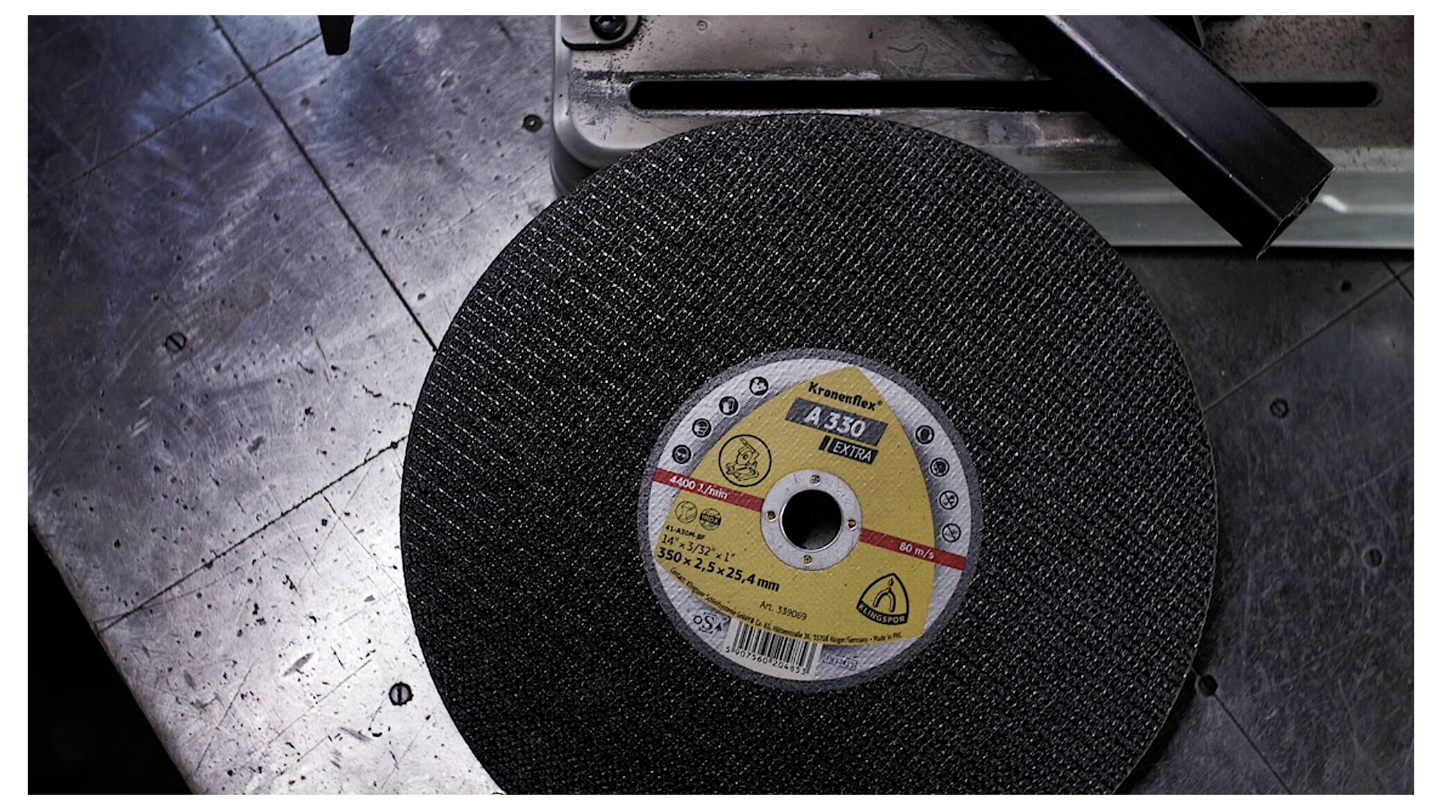 A metal-cutting disc labeled 'A30, 115x2.5x22.23mm' rests on a metallic workbench near a machinery component.