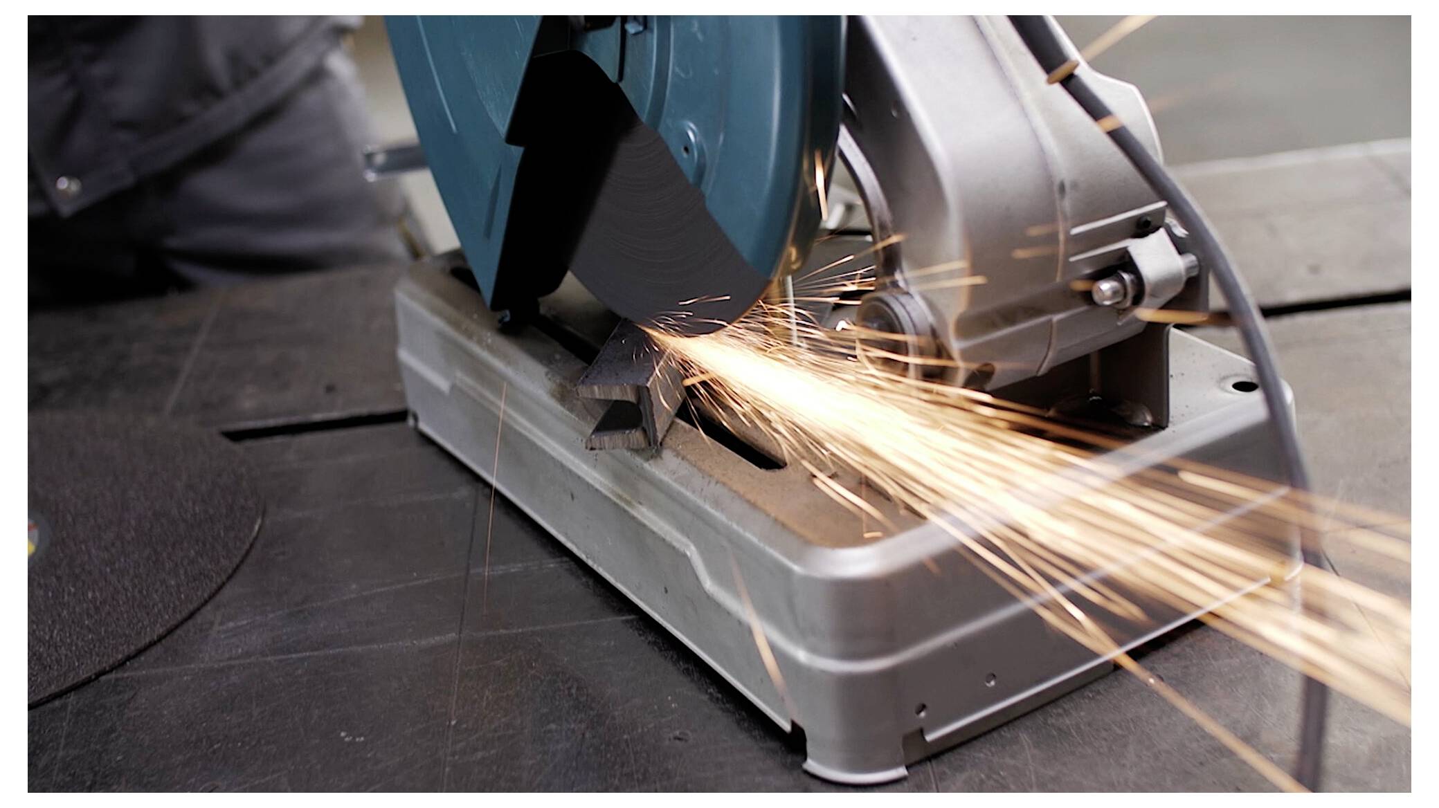 A metal cutting saw emits bright sparks as it cuts through a piece of metal, highlighting industrial activity and precision engineering.
