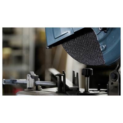 A close-up of a circular saw blade in a workshop, partially enclosed in a protective cover, with a metal clamping device in the foreground.