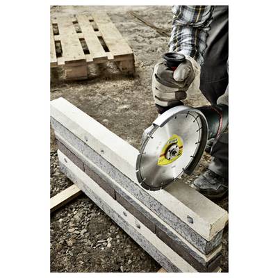 A person uses a power saw to cut a concrete block on a construction site, with wooden pallets in the background.