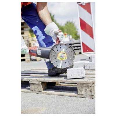 Worker using a circular saw to cut a concrete block on a wooden pallet at a construction site. Safety precautions, like gloves, are observed.