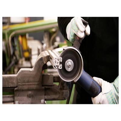 A person wearing gloves uses a blue angle grinder to cut a metal rail, held by a vise, in an industrial setting.