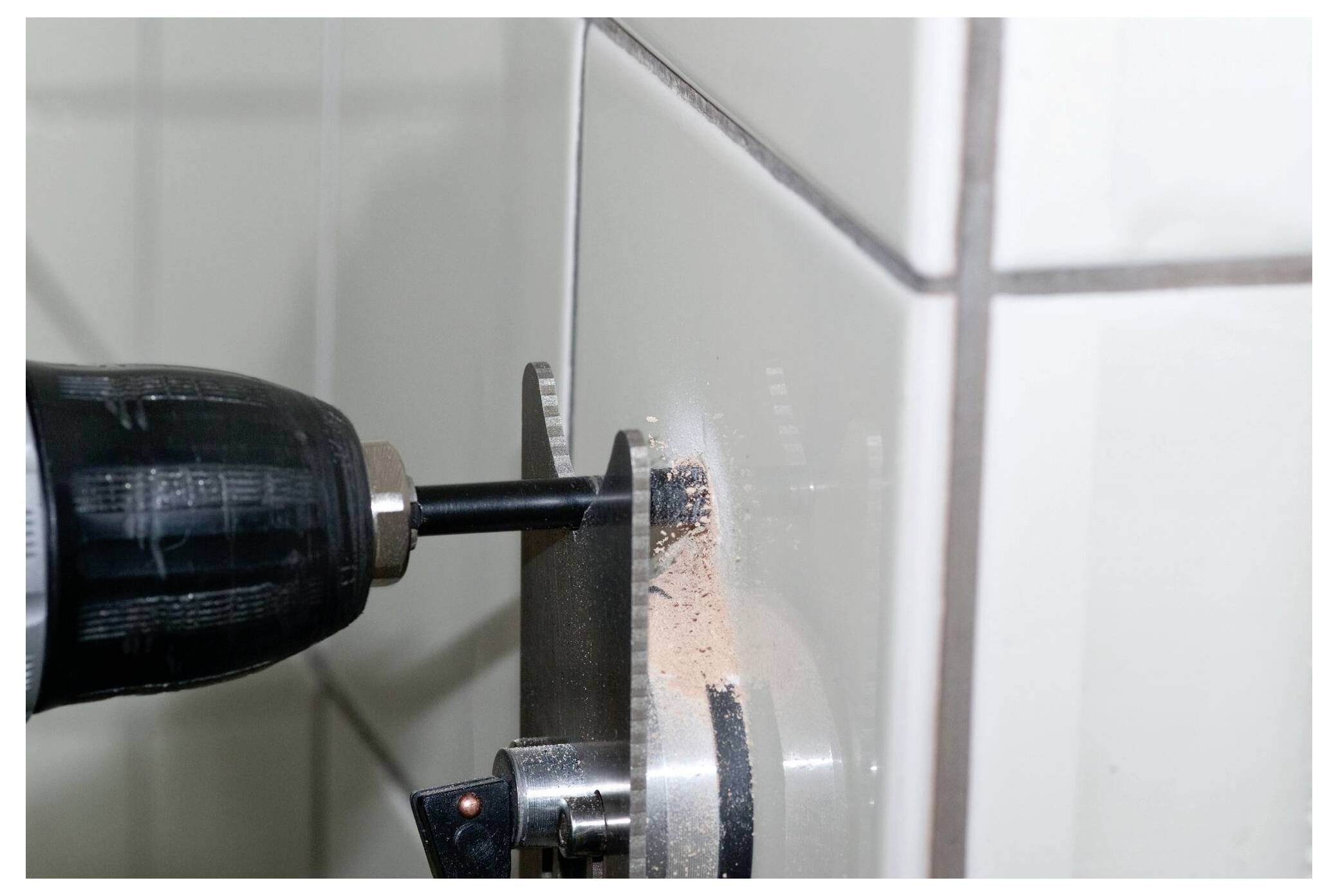 A drill creating a hole in a tiled wall, with dust particles visible around the drill bit.