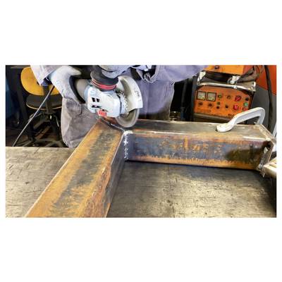 'Person using an angle grinder on a metal surface in a workshop, with a safety glove worn on the operating hand and industrial equipment in the background.'