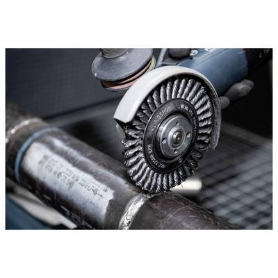 A power tool equipped with a wire brush attachment is polishing a metal pipe, smoothing the weld seam for a cleaner finish.