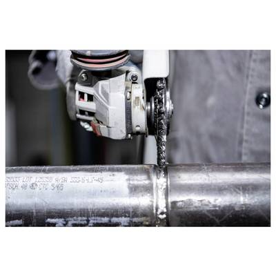 A person uses an angle grinder to cut through a metal pipe, wearing protective gloves. The grinder creates sparks during the cutting process.