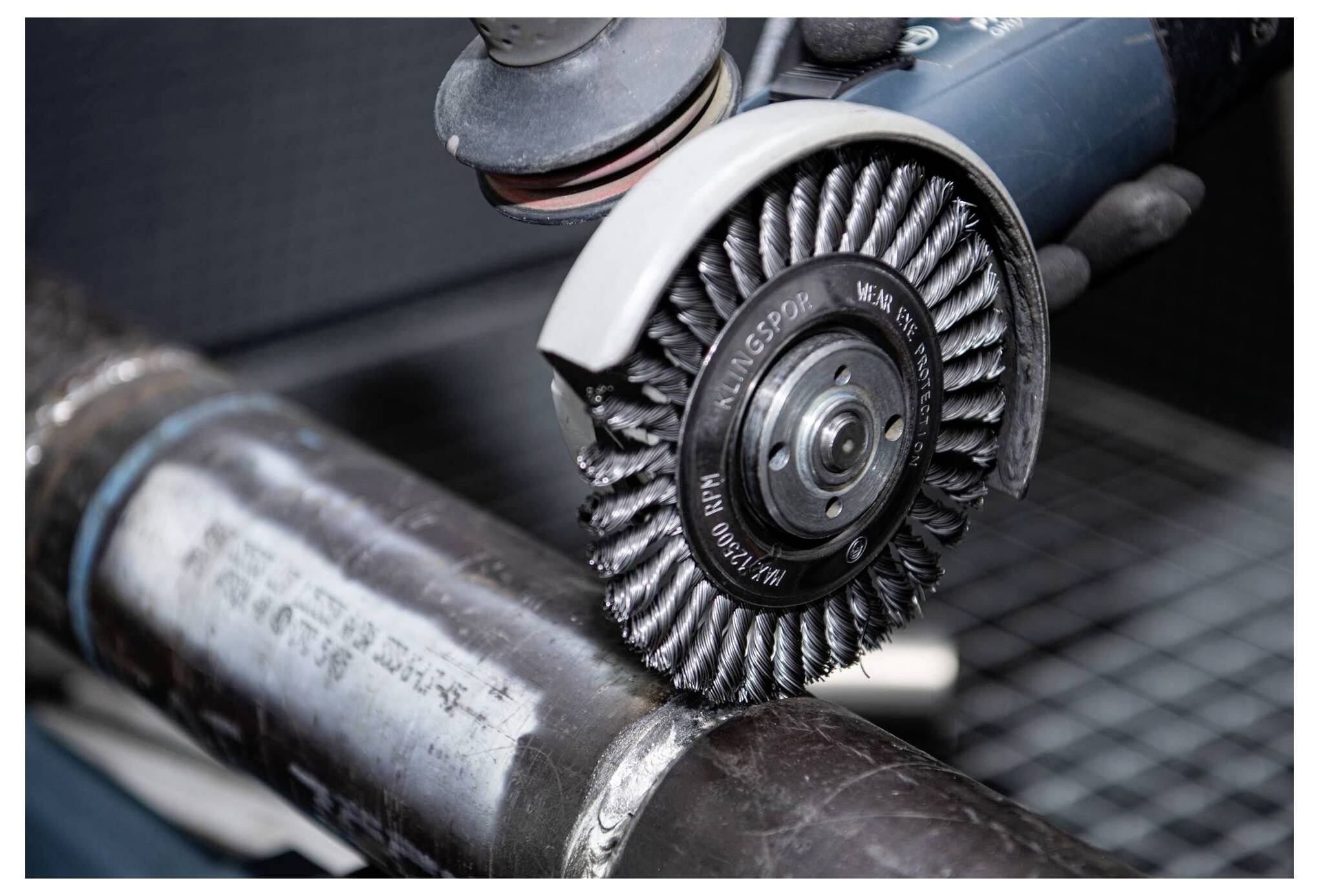 A power tool with a wire brush attachment is used to clean and polish the surface of a metal pipe.