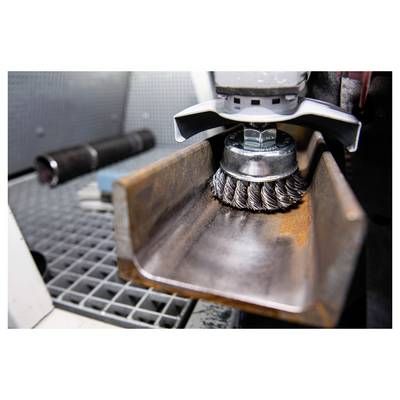 'A close-up of a power tool with a wire brush attachment cleaning rust from a metal beam in a workshop setting.'