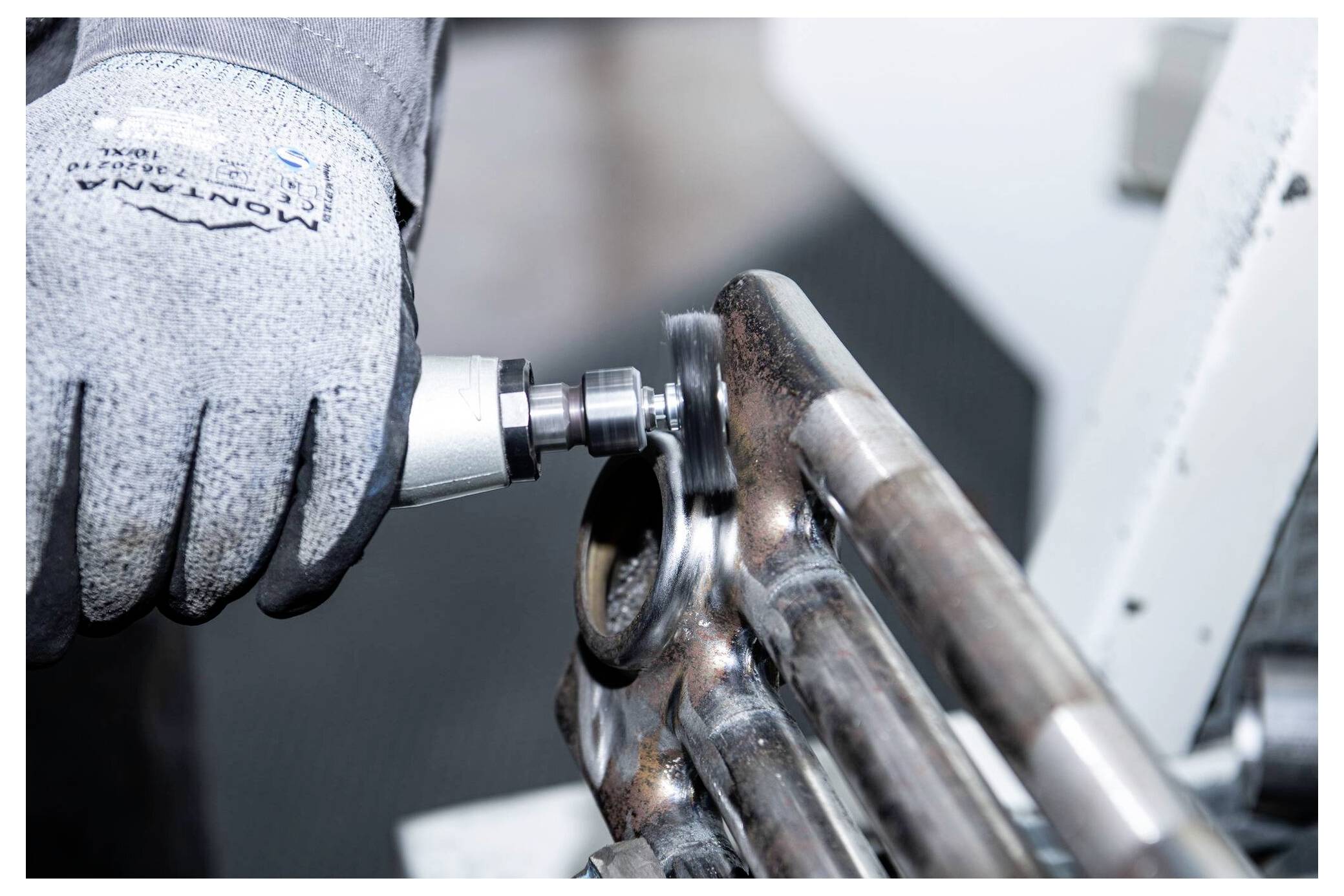 A person wearing work gloves uses a power tool to polish metal pipes in an industrial setting.