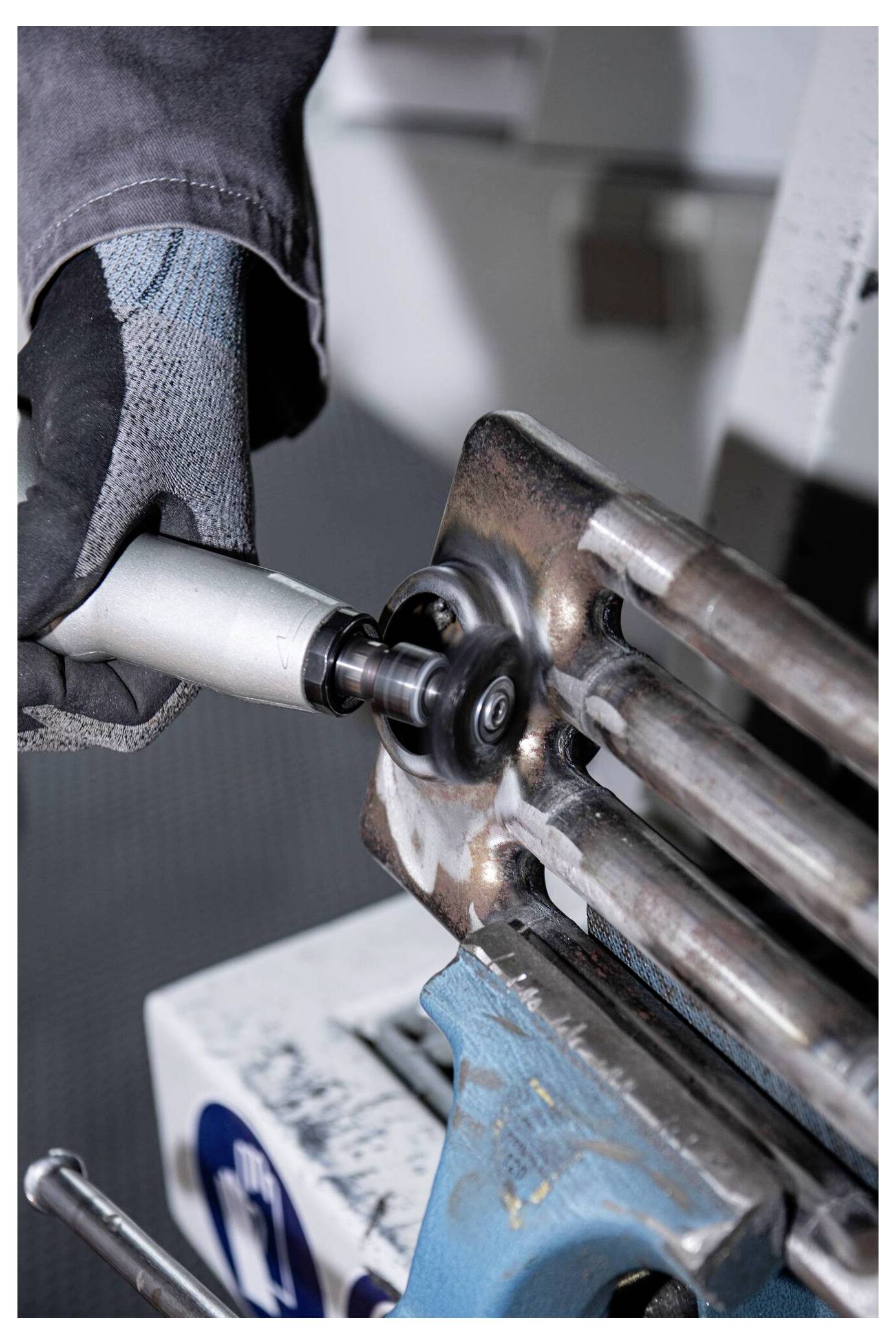 A person wearing a protective glove uses a handheld power tool to grind metal bars. The scene suggests metalworking or fabrication.