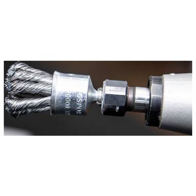 A close-up of a metal wire brush attachment connected to a power tool, used for cleaning or polishing surfaces, in action.