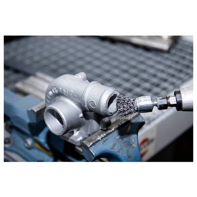 A metal component being cleaned with a wire brush attachment on a drill, secured in a vise on a workbench.