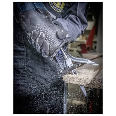 A person using a power saw to cut through wood, wearing protective gloves and work clothes. Sawdust is visible in the air around the cutting area.