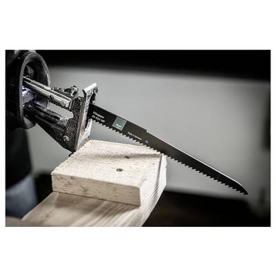 A long serrated saw blade extends from a clamp, set against a wooden block. The setting suggests woodworking or carpentry activities.