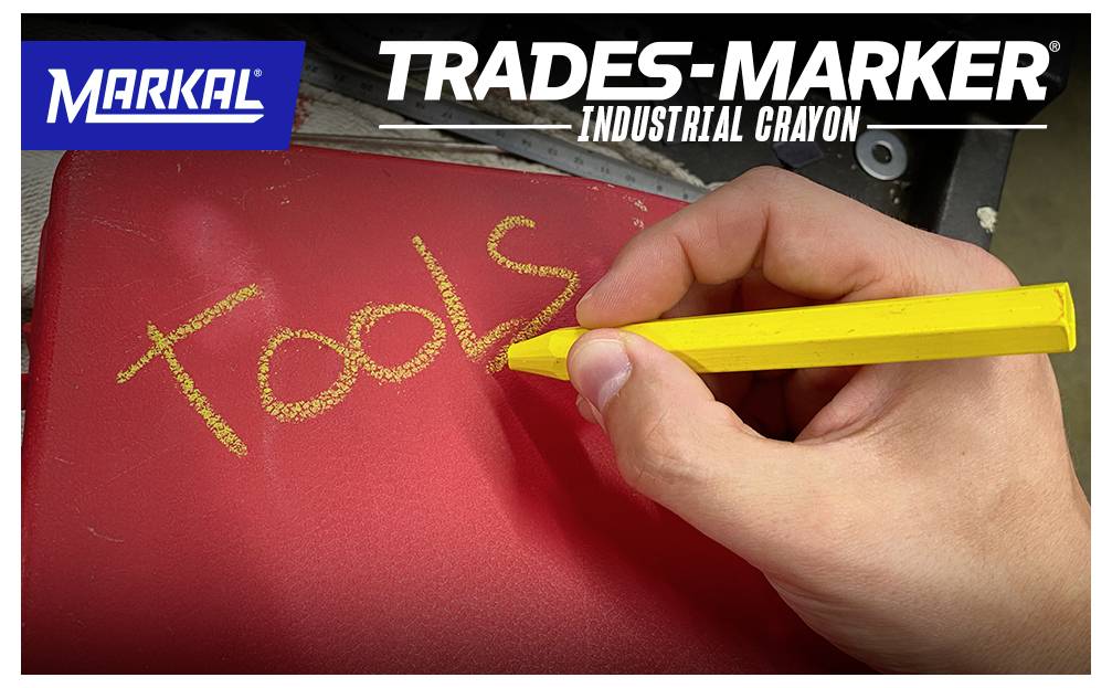 'A hand writing the word "Tools" on a red surface using a yellow industrial crayon. Branding text reads: Markal Trades-Marker Industrial Crayon.'