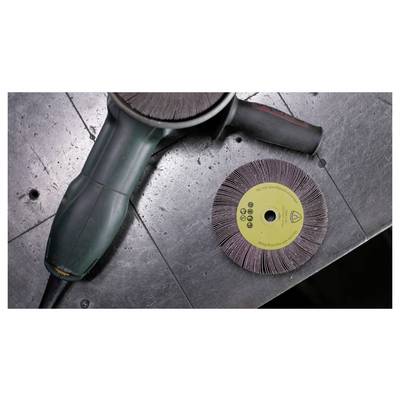 An electric angle grinder with a flap disc attached sits on a metallic surface next to an unused similar disc.