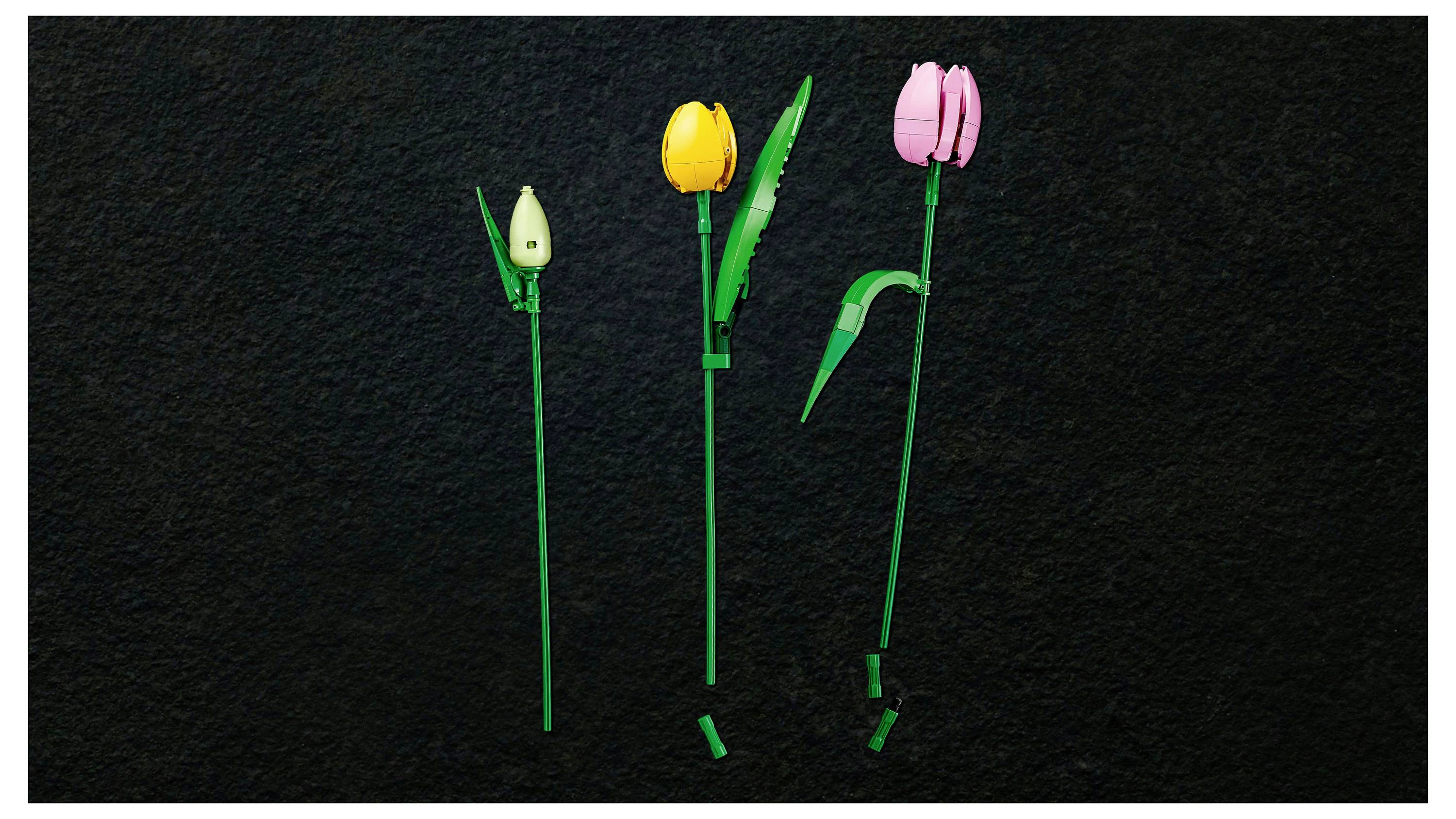 Three LEGO flower stems: one with a green bud, one with a yellow bloom and green leaves, and one with a pink bloom. Black background.