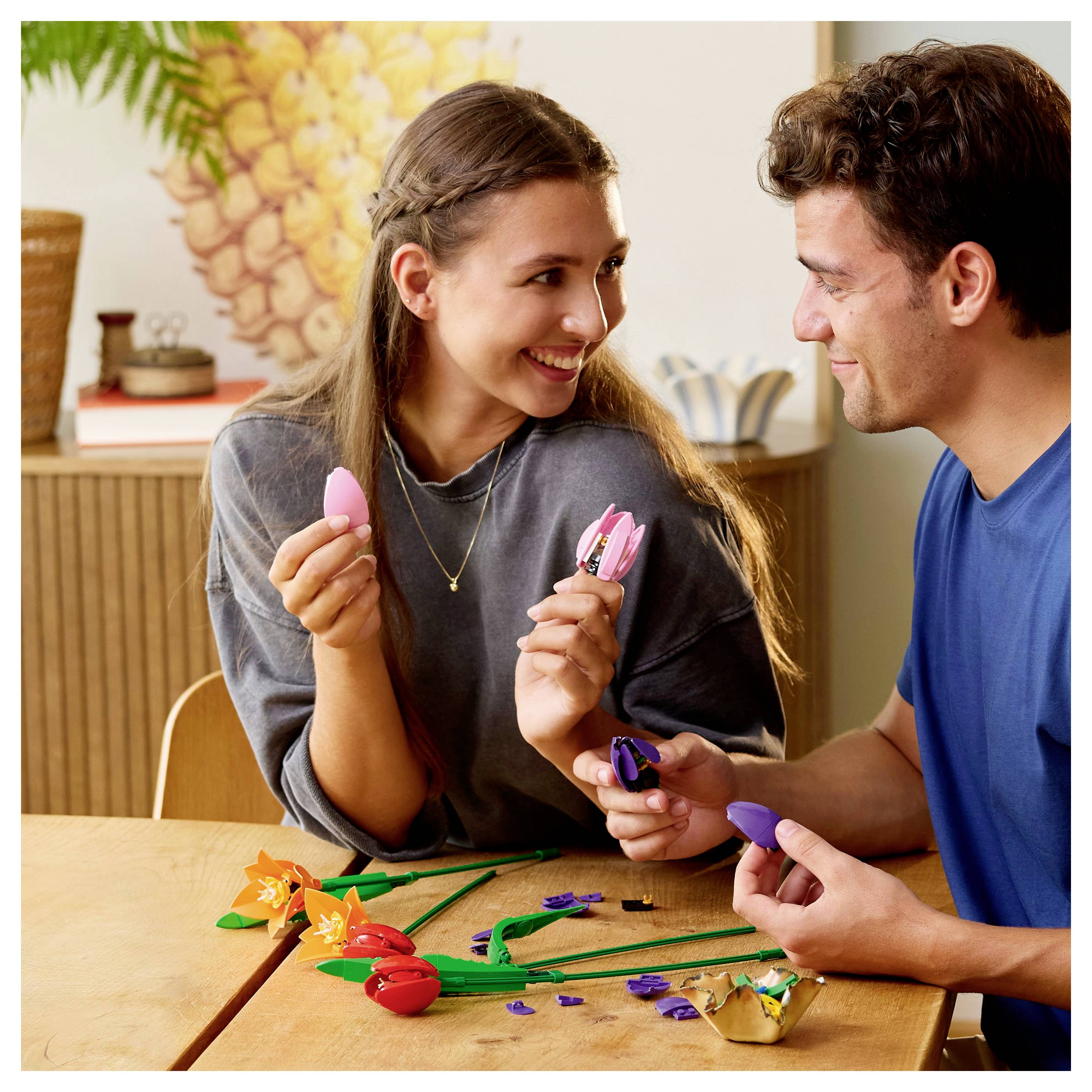 A smiling woman and man are sitting at a table, exchanging colorful egg-shaped toys, with a playful atmosphere.