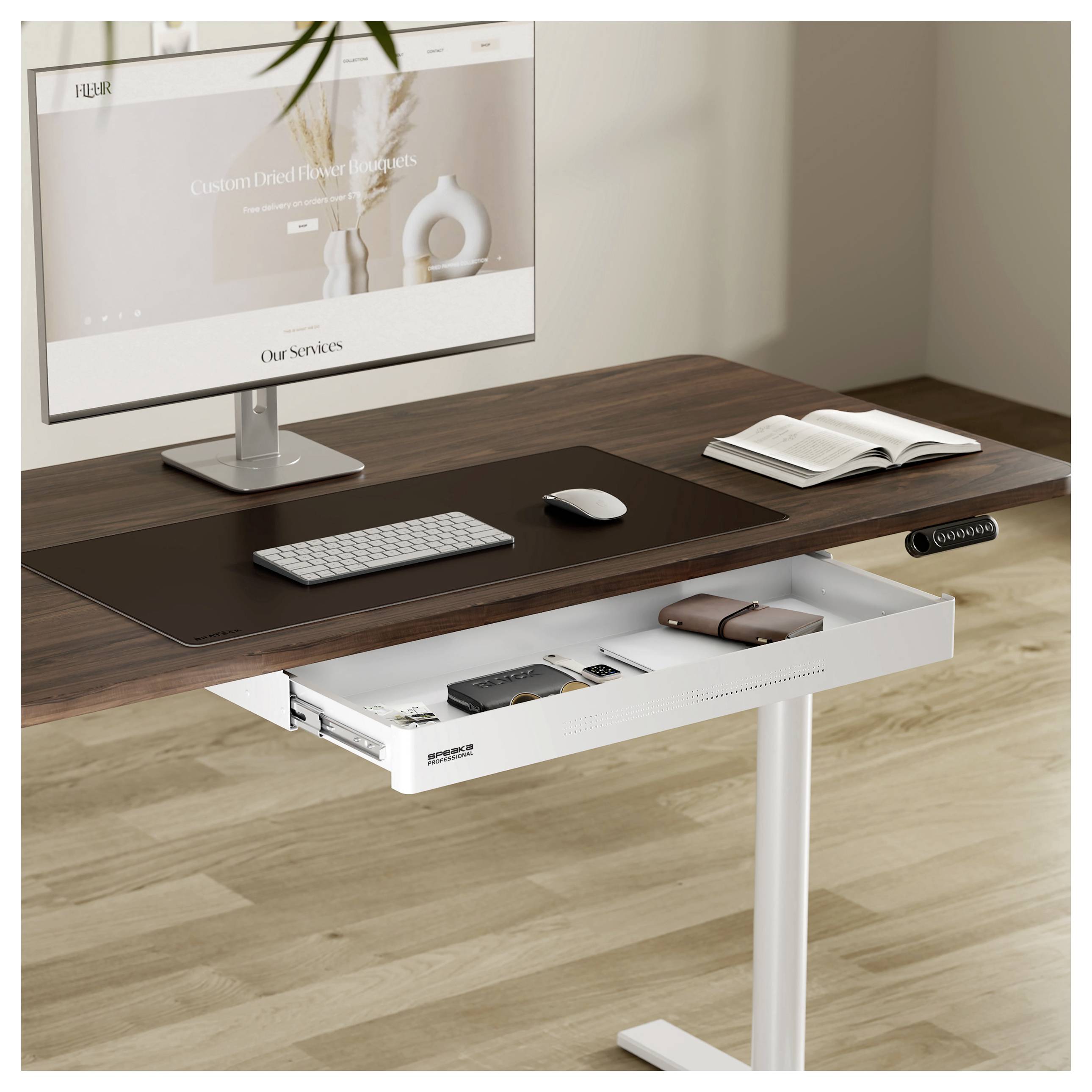 A modern workspace with a wooden desk featuring a computer screen, keyboard, and an open drawer containing a notebook and tech accessories.
