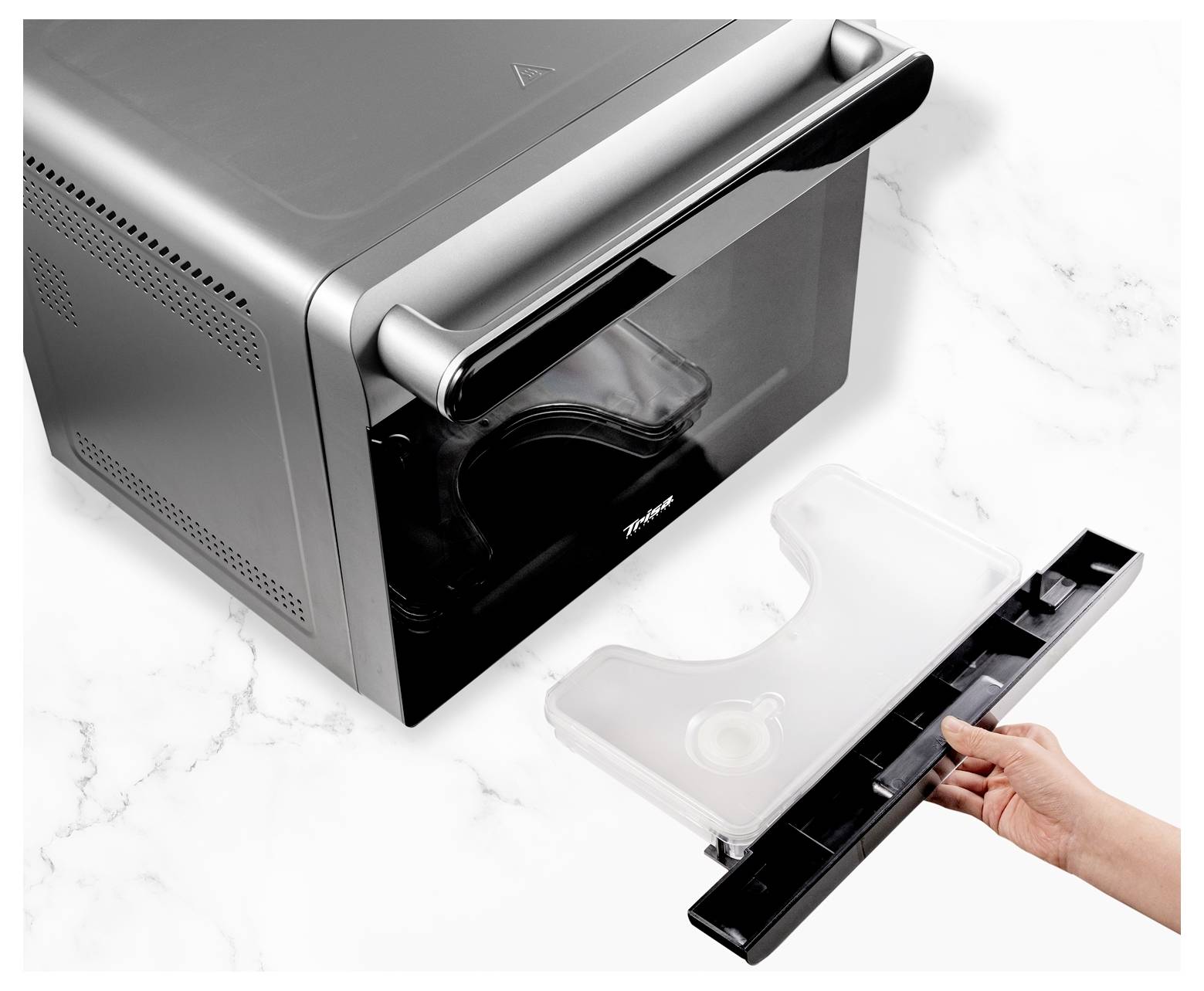 A person is removing a transparent plastic tray from a black appliance on a white marble surface.