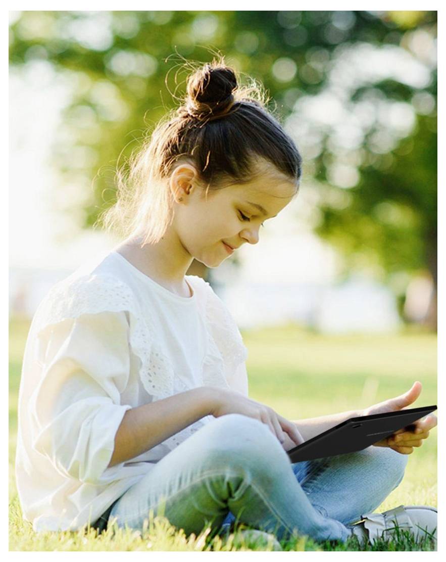 A young girl sits on grass in a park, focused on a tablet. She smiles slightly, the sunlight filtering through trees in the background.