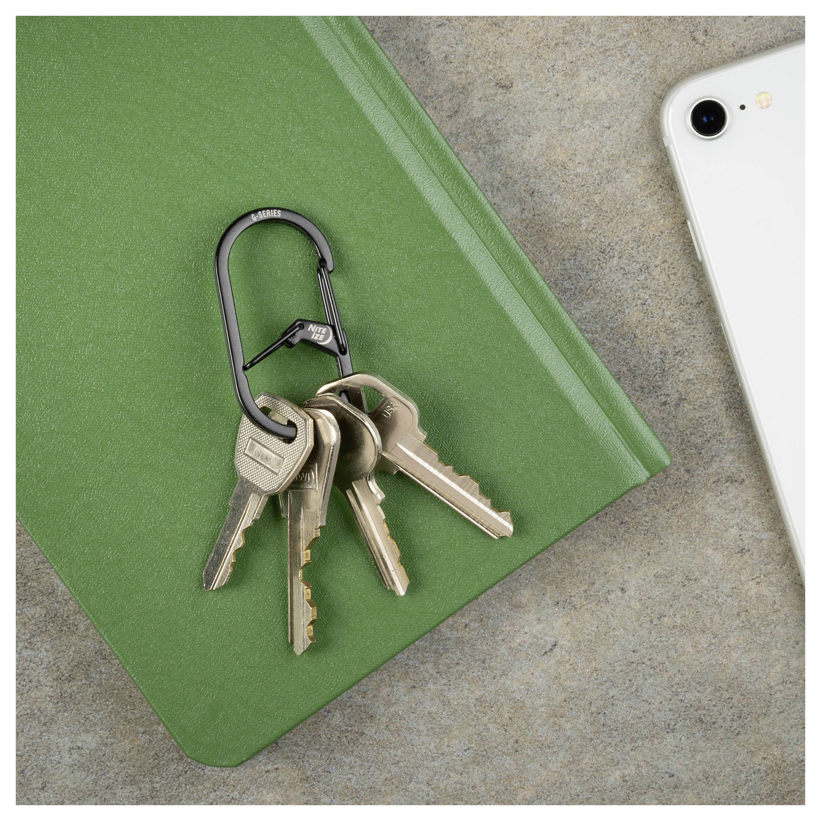 A set of three keys on a black carabiner, resting on a closed green book, with the corner of a smartphone visible on a gray surface.
