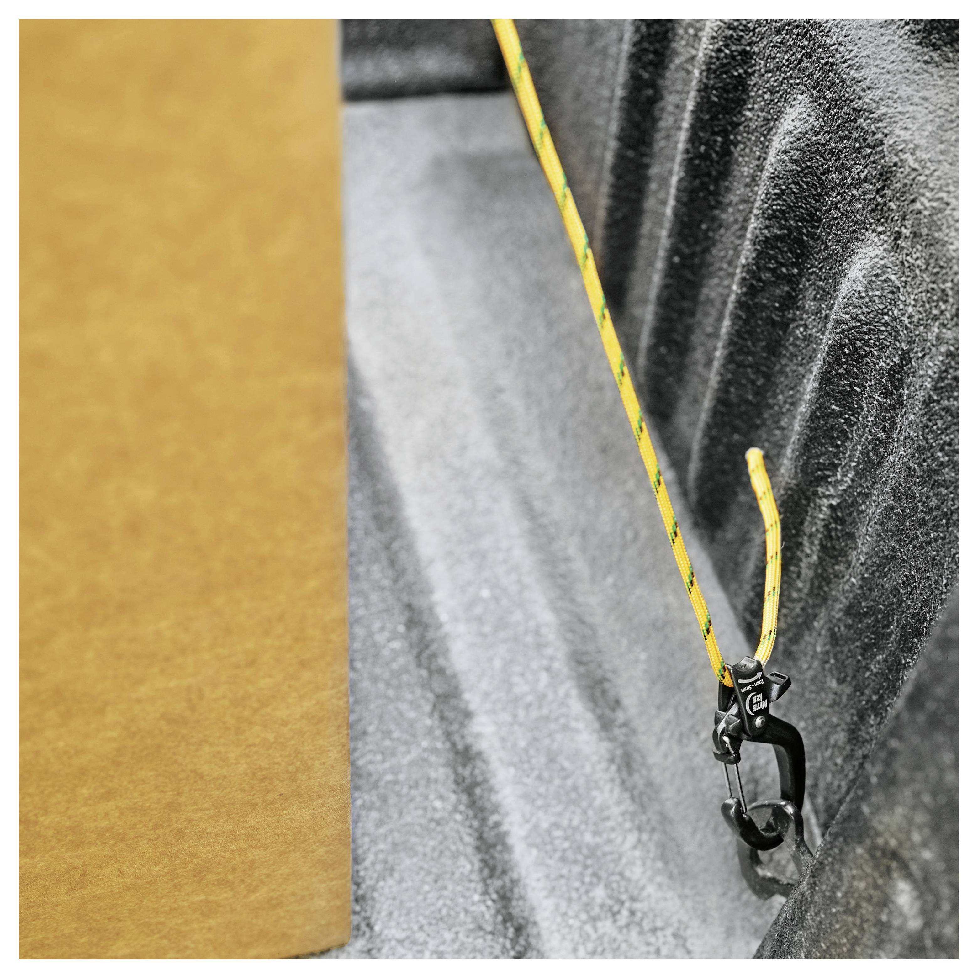 A yellow bungee cord with black hooks, securely fastened to a metal loop inside a truck bed with textured surfaces and a cardboard piece on the left.