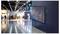 A large digital display with colorful graphs is mounted on a wall in a modern, spacious exhibition hall with blurry visitors in the background.