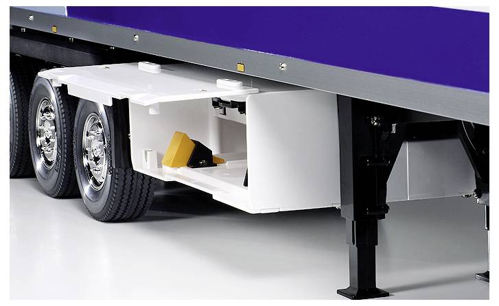 A truck trailer with a white storage compartment open, revealing a yellow wheel chock inside. The trailer has shiny dual wheels.