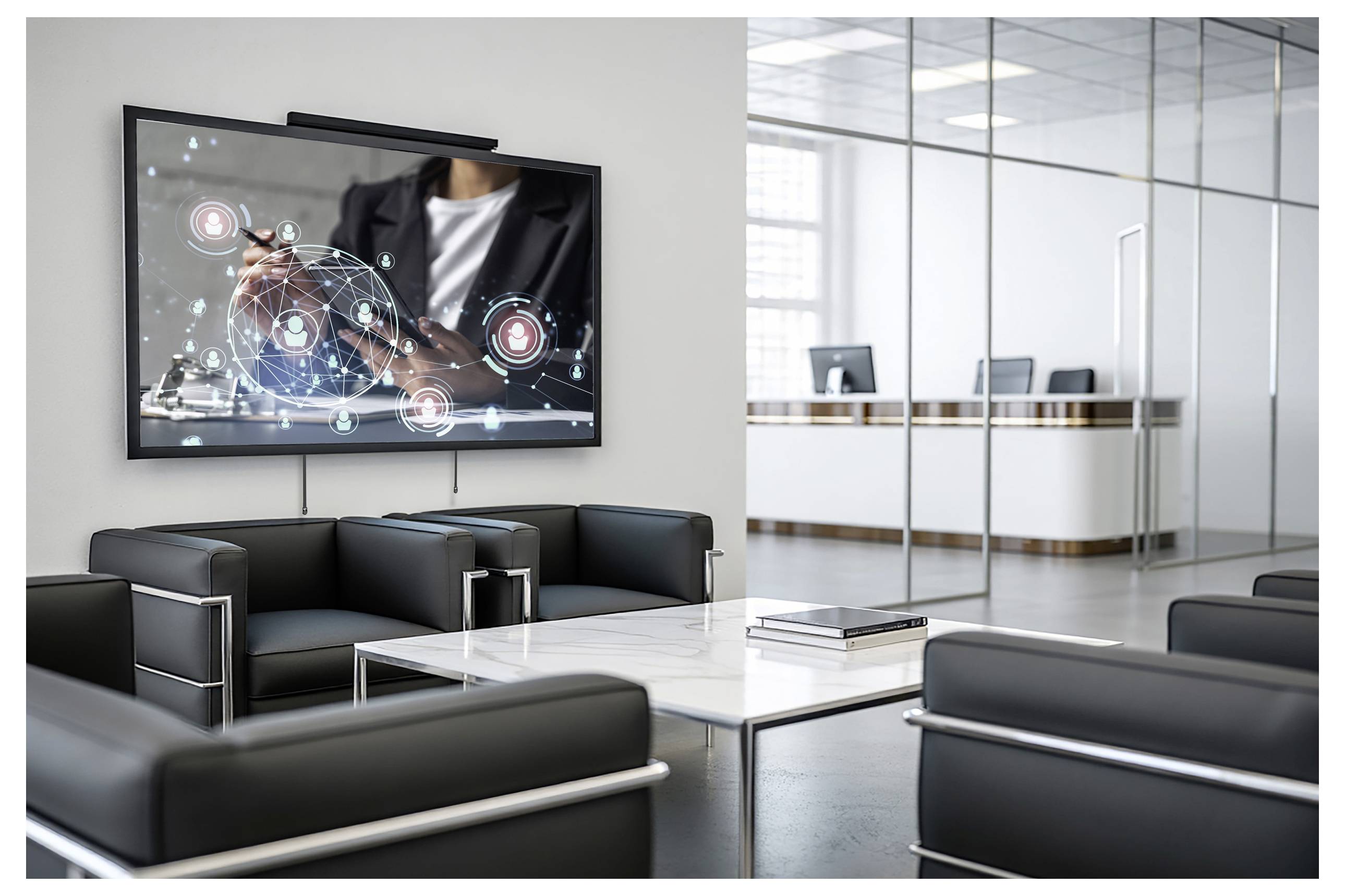 A modern office lounge with black leather sofas, a marble coffee table, and a digital screen displaying hands interacting with virtual graphics.