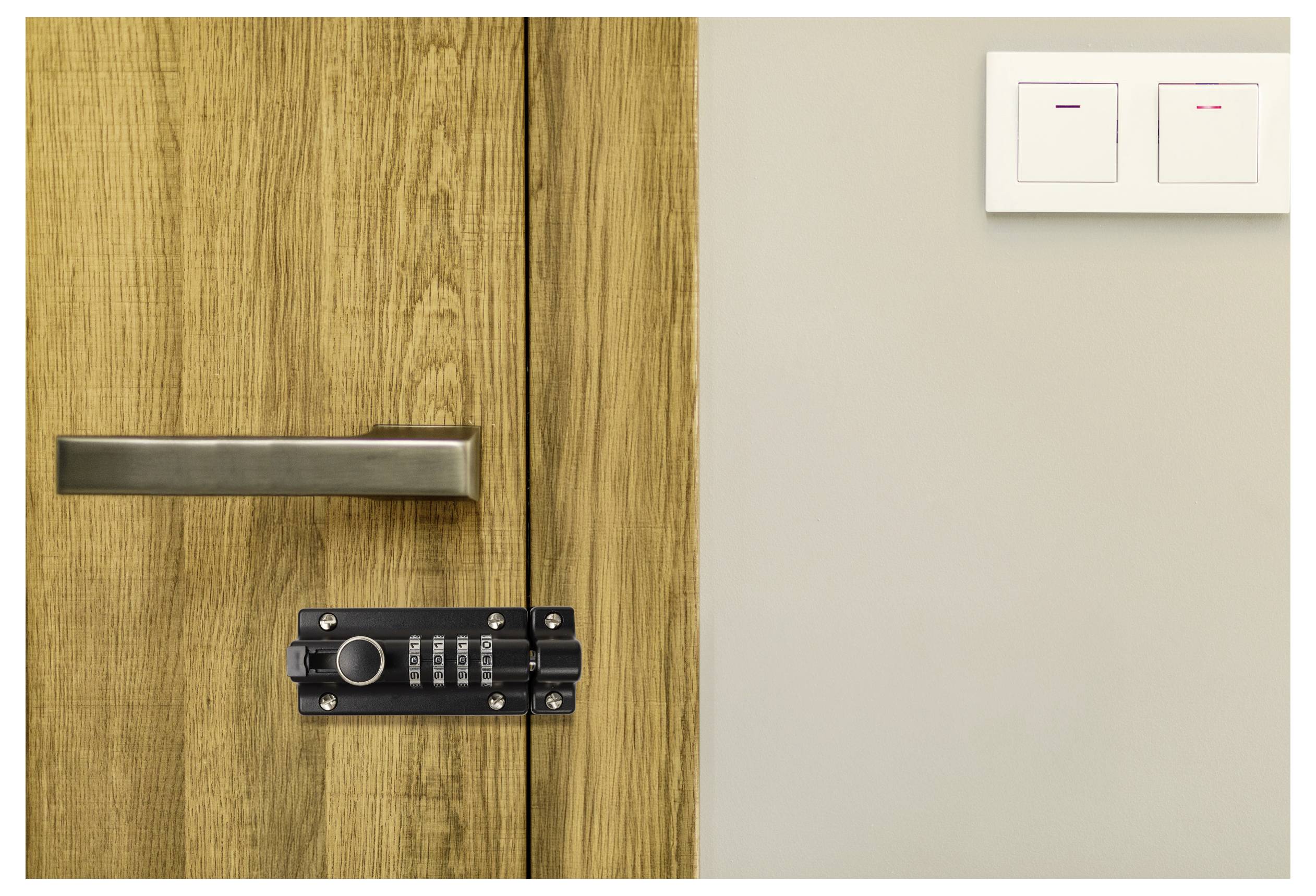 A locked wooden door with a handle and a numeric keypad lock next to a dual light switch on a beige wall.