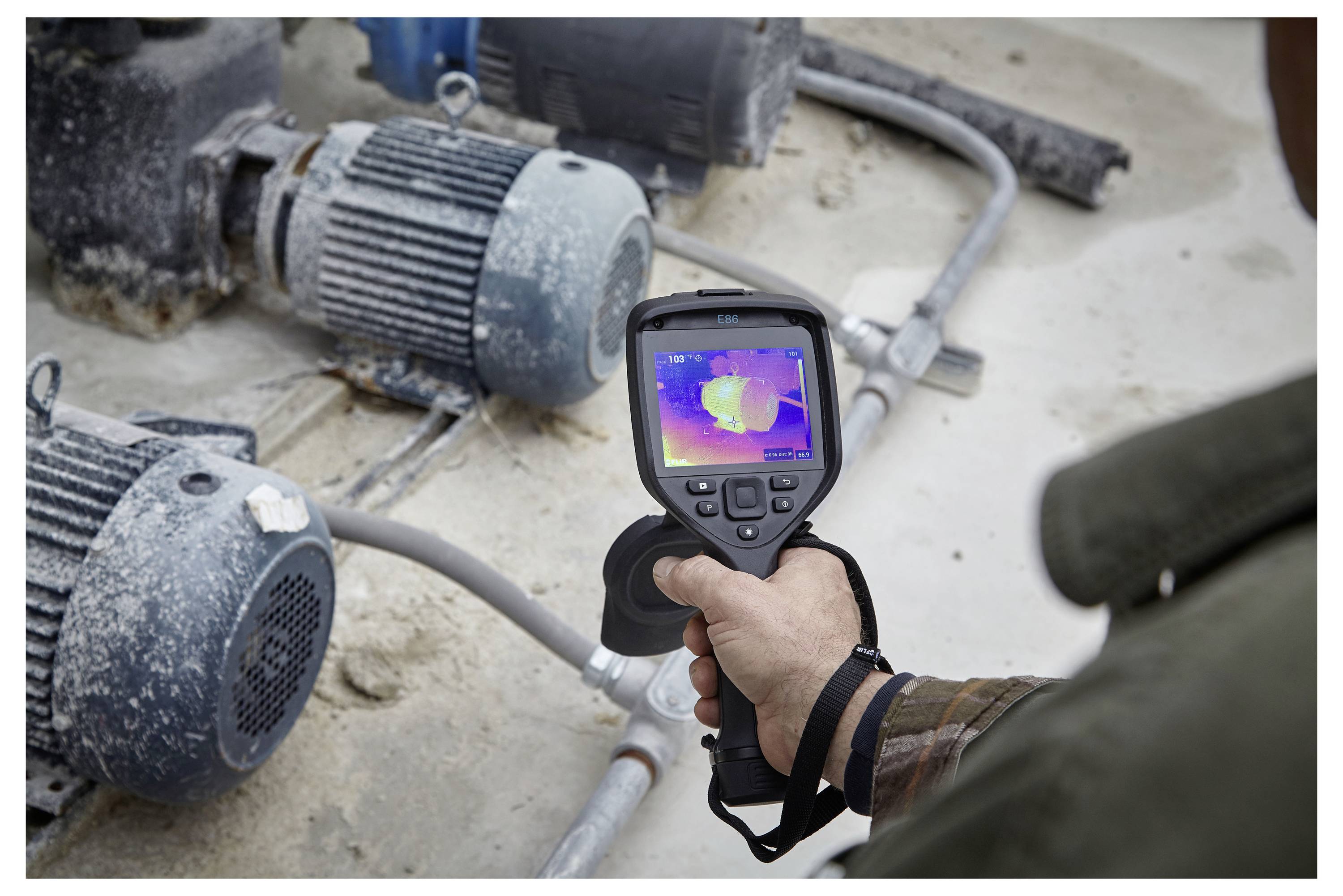 A person uses a handheld thermal imaging camera to inspect machinery for heat irregularities, displaying a color-coded heat map on the screen.