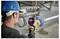 A person wearing a blue hard hat uses a handheld thermal imaging device to inspect pipes in an industrial setting.