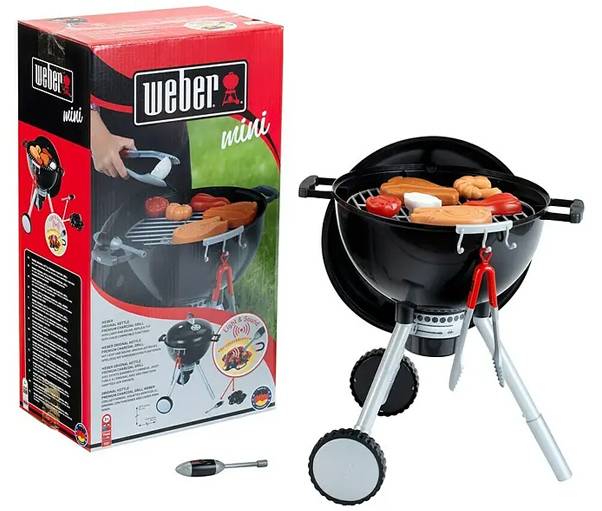 'Weber mini' toy grill set with box. Features a black grill on a stand with play food items like sausages and tongs included.