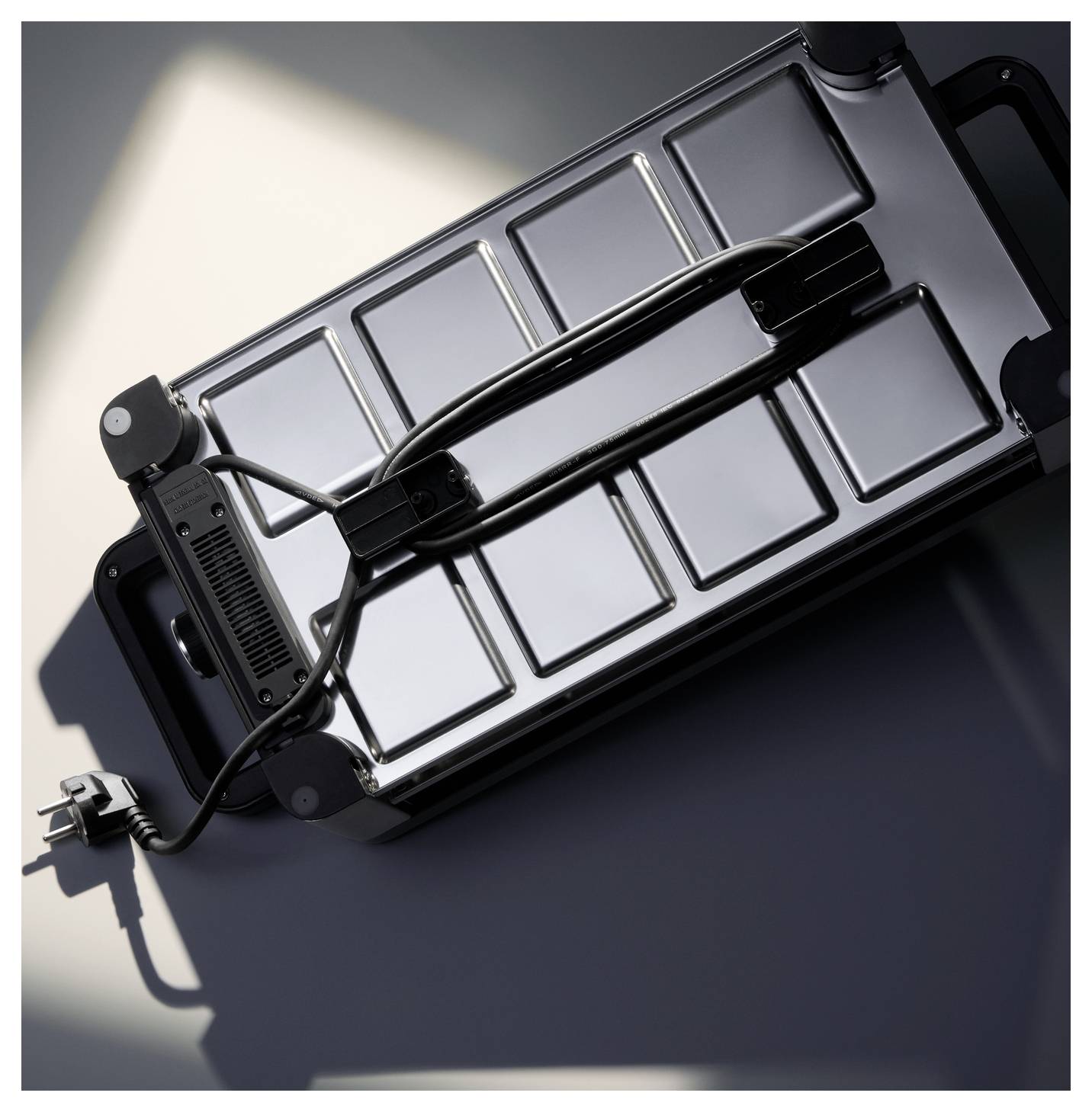 A silver suitcase with black handles and an attached power cord lies on its side, casting a shadow on the ground.
