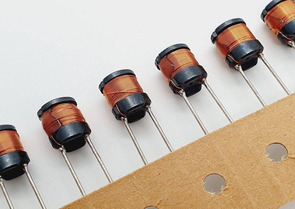 A close-up of several diodes with copper wire wrapping, arranged in a row on a strip of cardboard, showcasing electronic components.