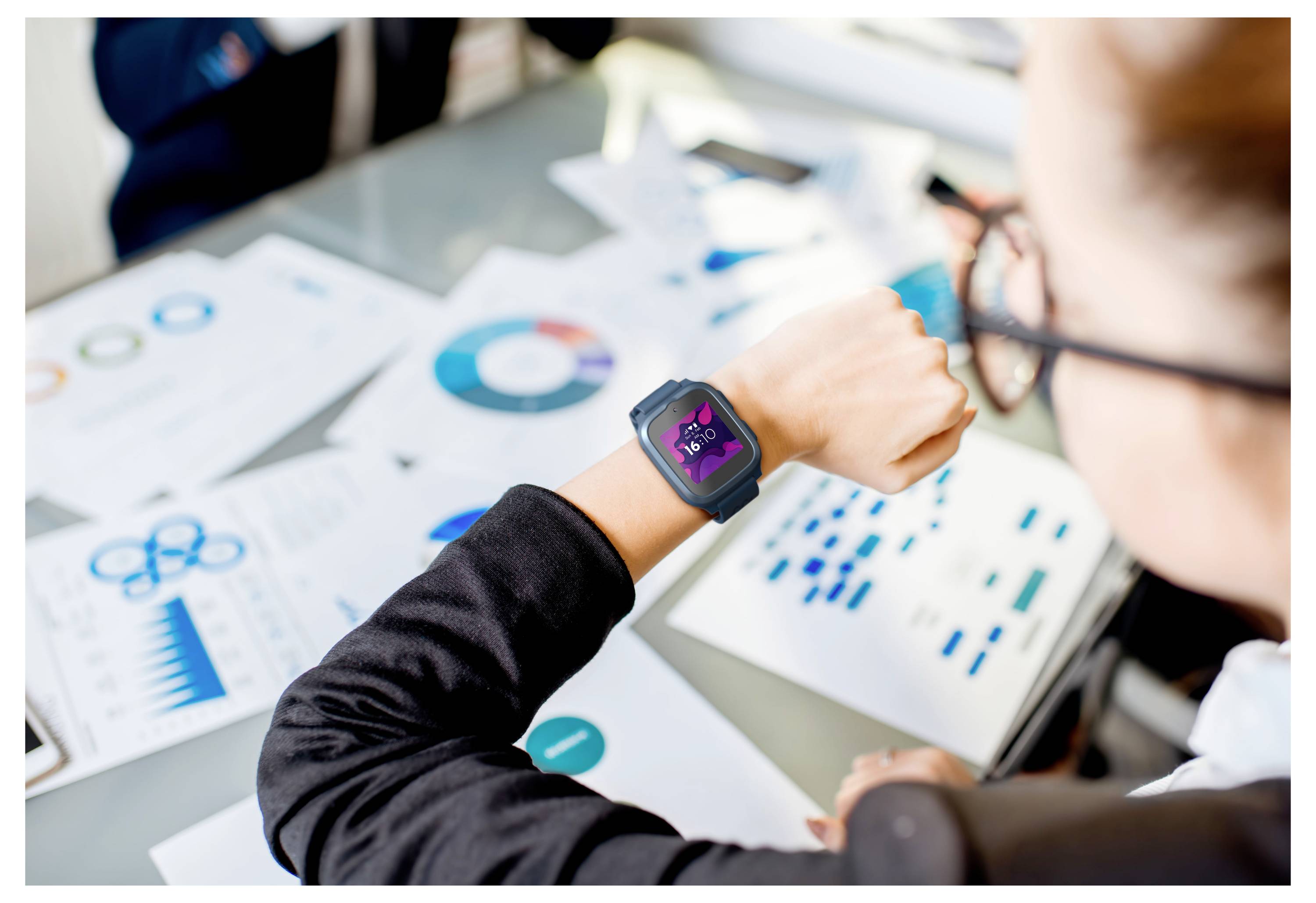 A person in a business suit checks the time on a smartwatch displaying '5:40' over a table filled with various business charts and graphs.