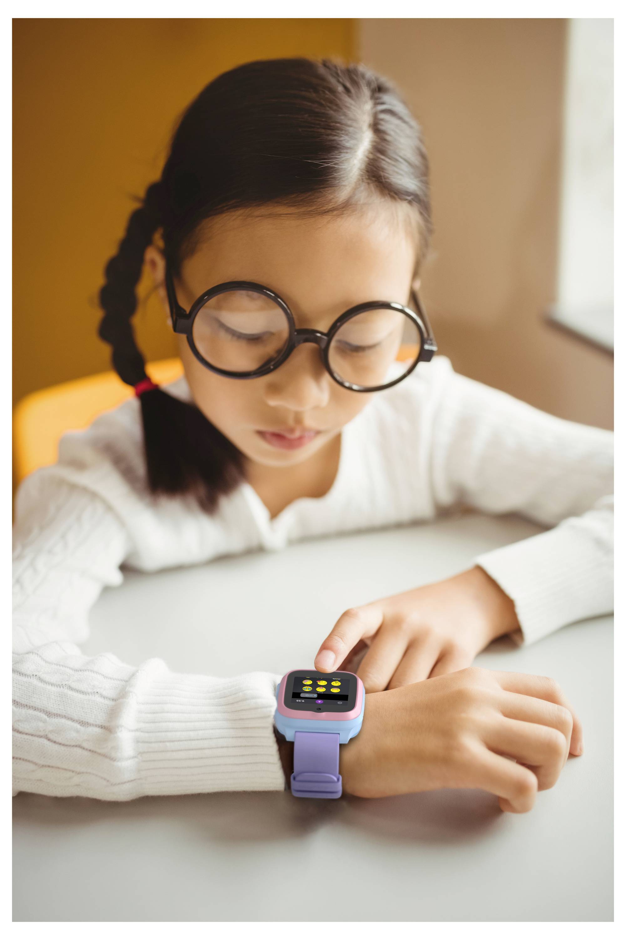 A young person with glasses looks at a smartwatch on their wrist at a table, appearing focused on the device's screen.