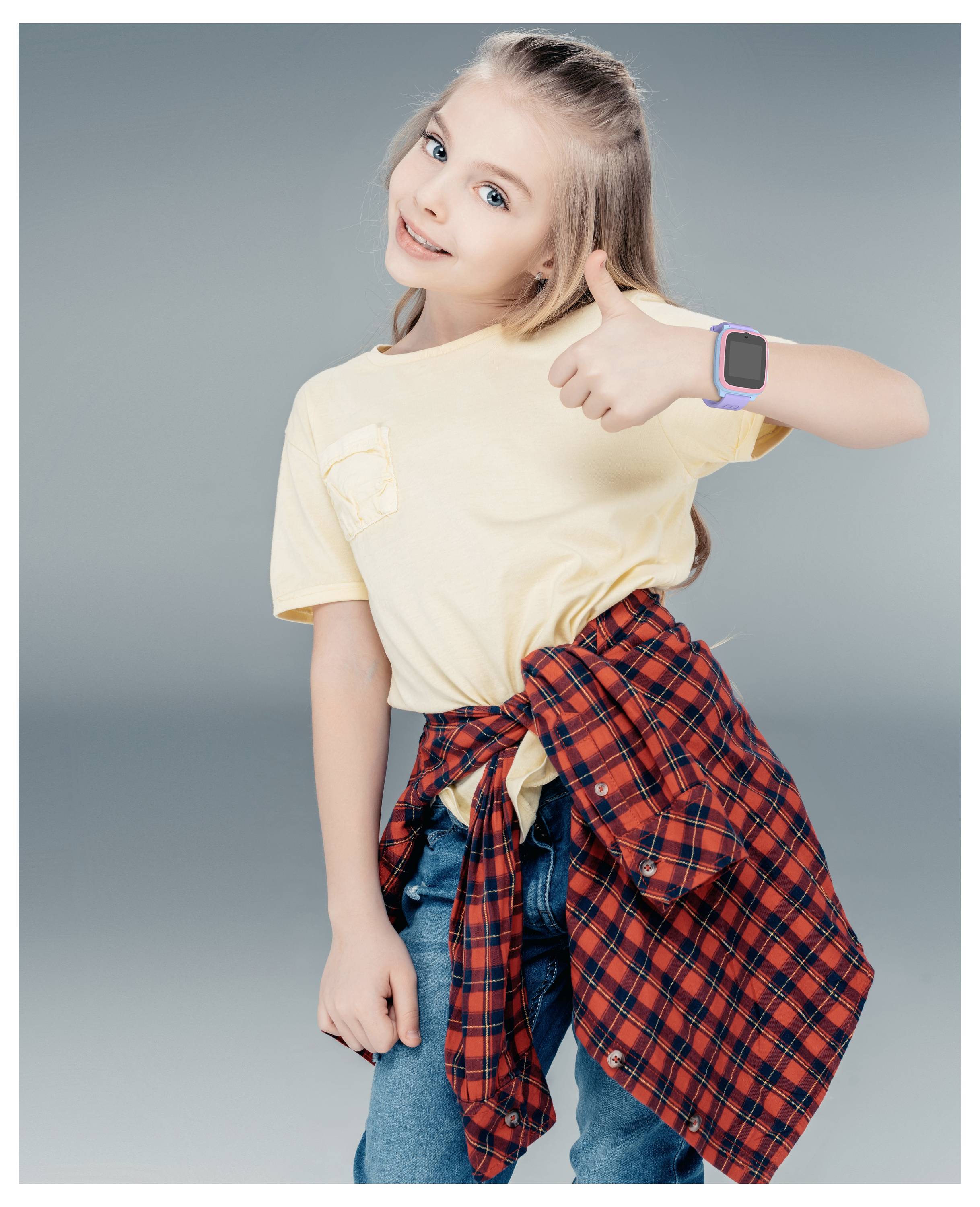 A young girl smiling and giving a thumbs up, wearing a yellow shirt and a red checked shirt tied around her waist.