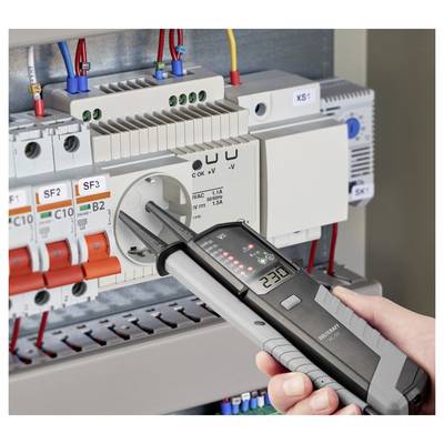 Handheld electrical tester measuring an electrical panel, with probes inserted into a socket near circuit breakers and wiring.