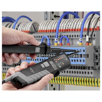 Hands testing an electrical control panel with two voltage/current measuring devices among wired terminal blocks and circuit connections.