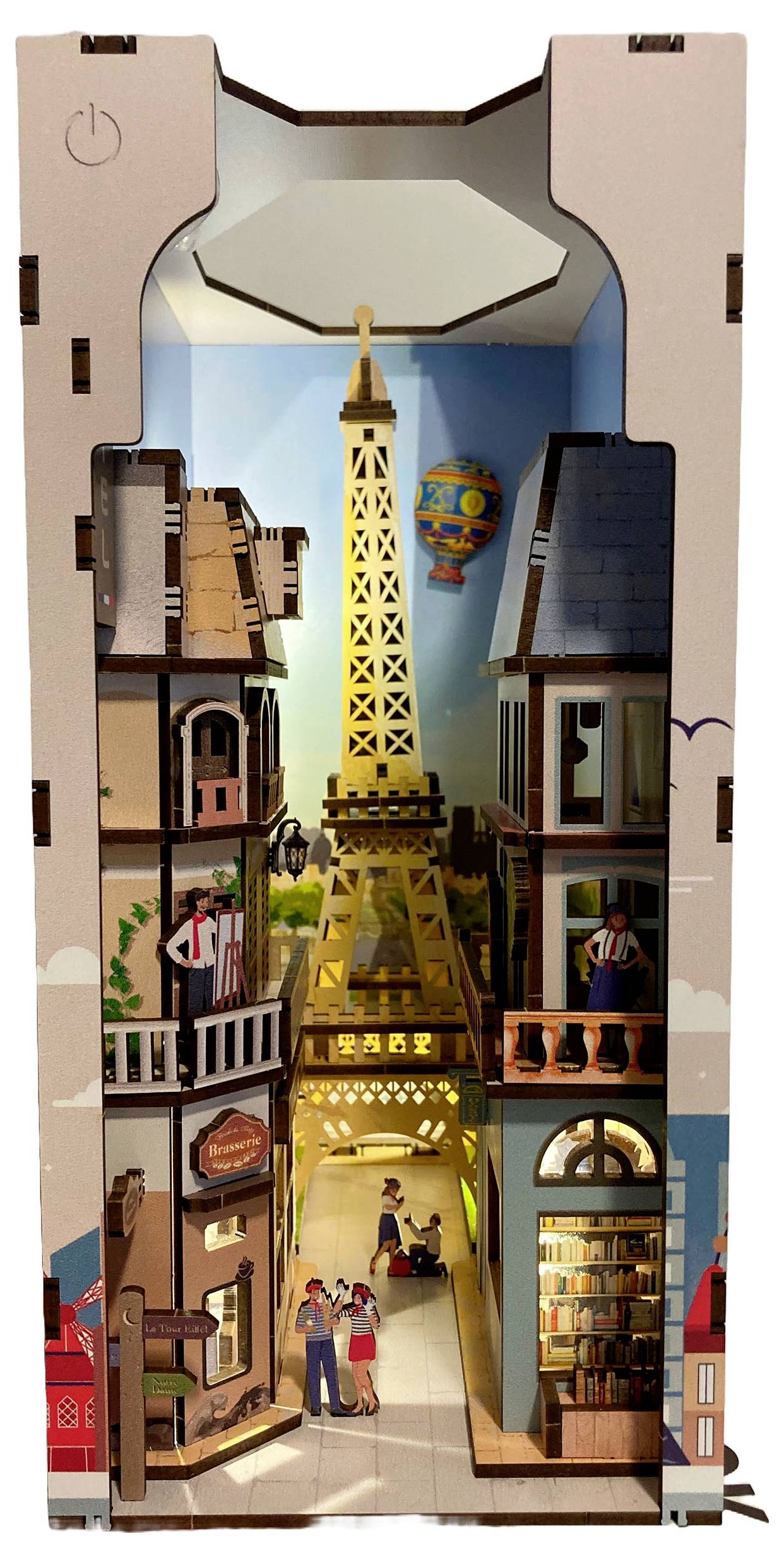 Cardboard tower model with cutouts of Parisian buildings and the Eiffel Tower centered. A small hot air balloon floats in the background.