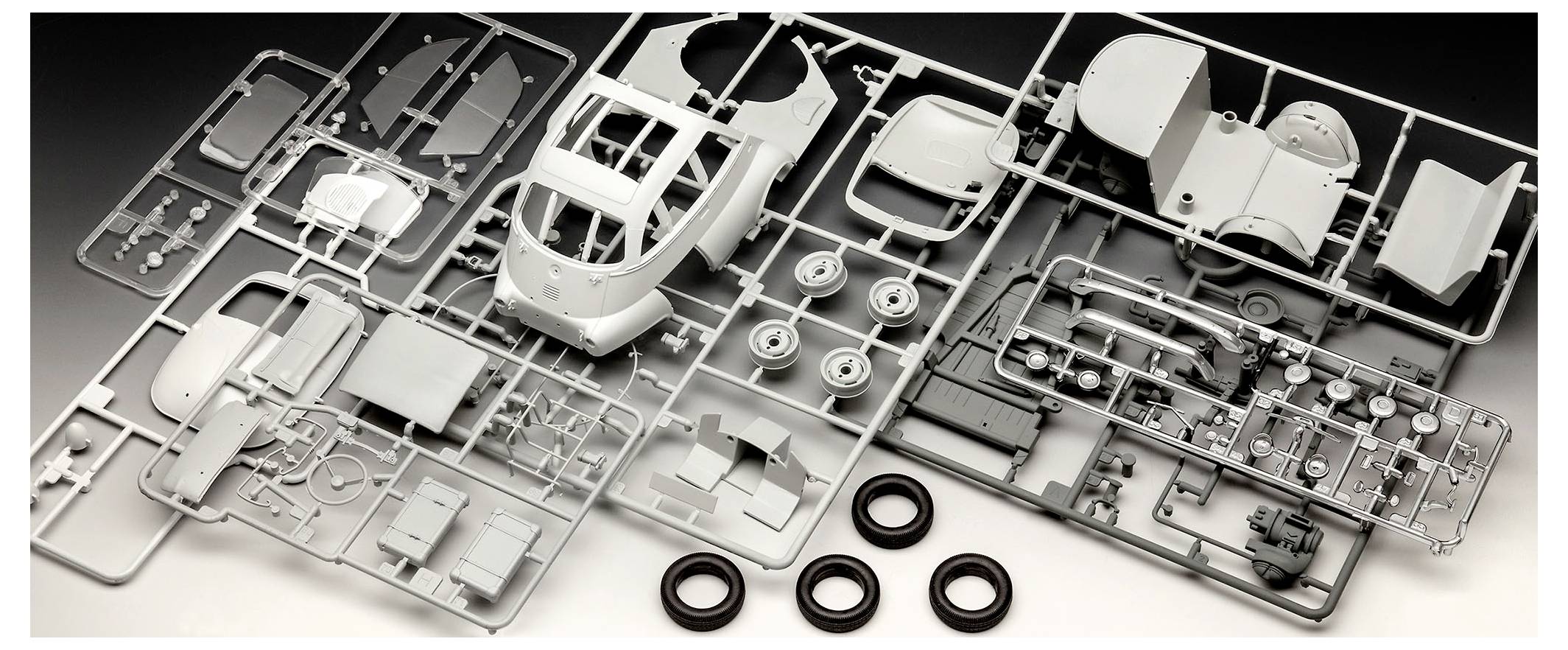 Model kit parts laid out on sprues, showing components for assembling a scale model vehicle, including wheels, body sections, and various detailed parts.
