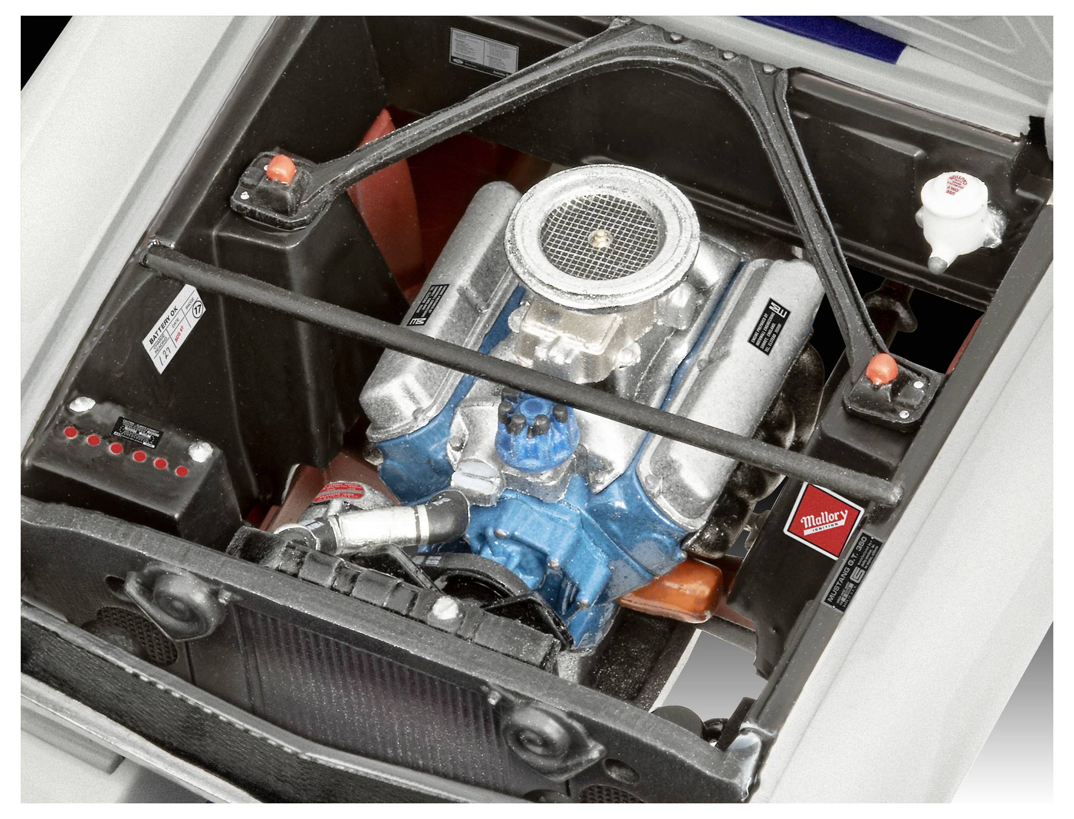 A close-up view of a car engine covered with various silver and blue components, surrounded by metallic supports and small labels.