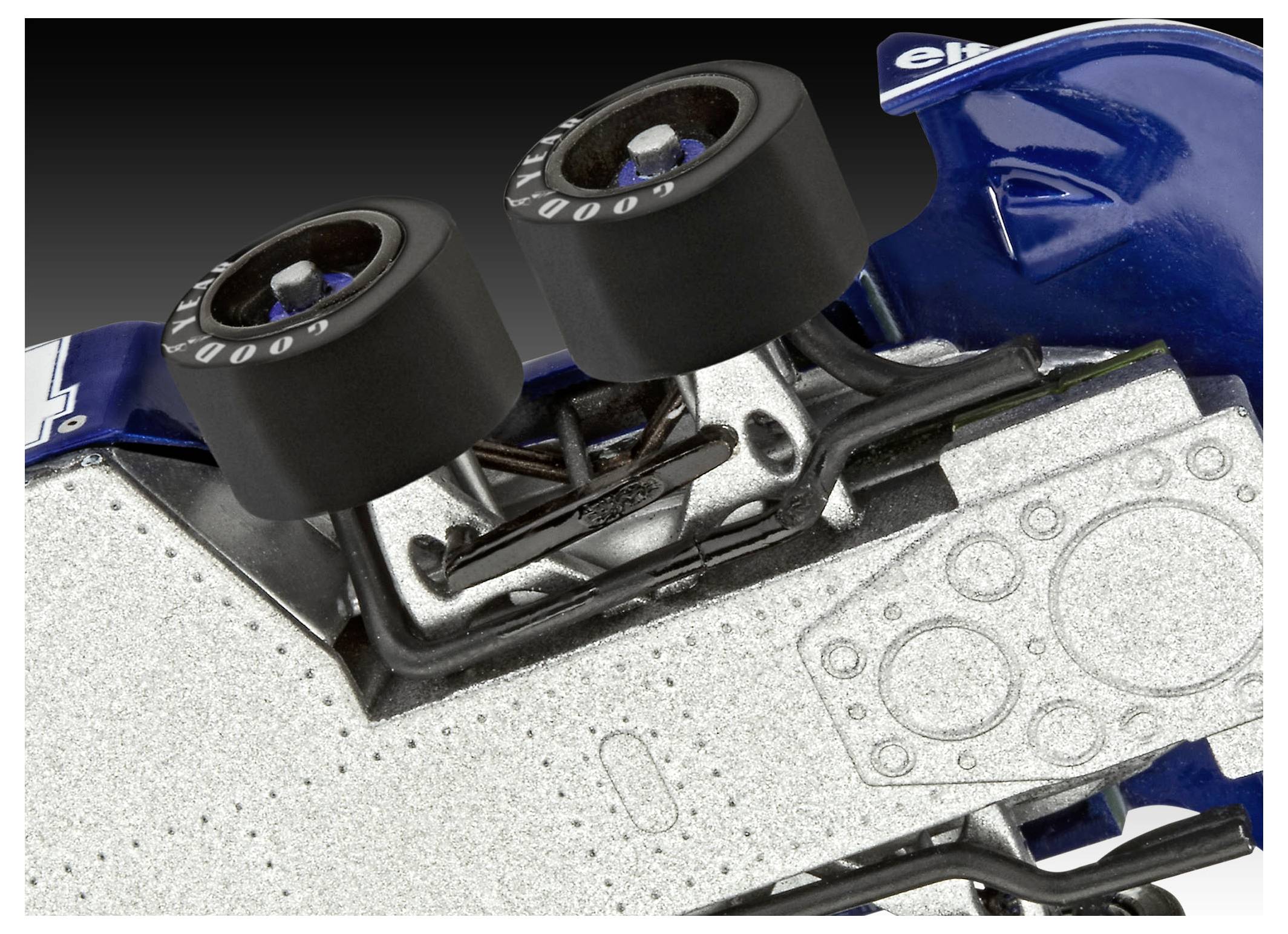 Close-up of a toy car's underside, showing detailed wheel and chassis components. The car is blue with a textured metallic surface.