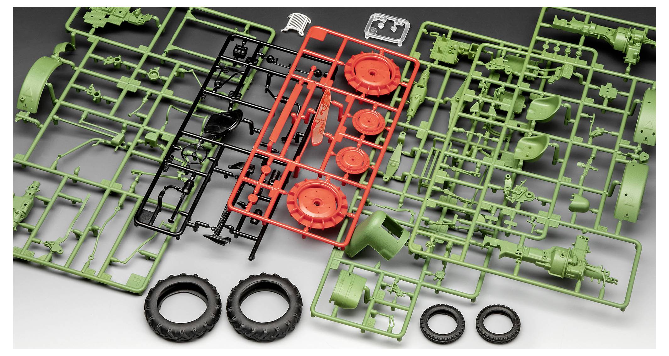 Plastic model kit parts for a tractor, spread out on a surface, including wheels, axles, and body components in green, red, and black.