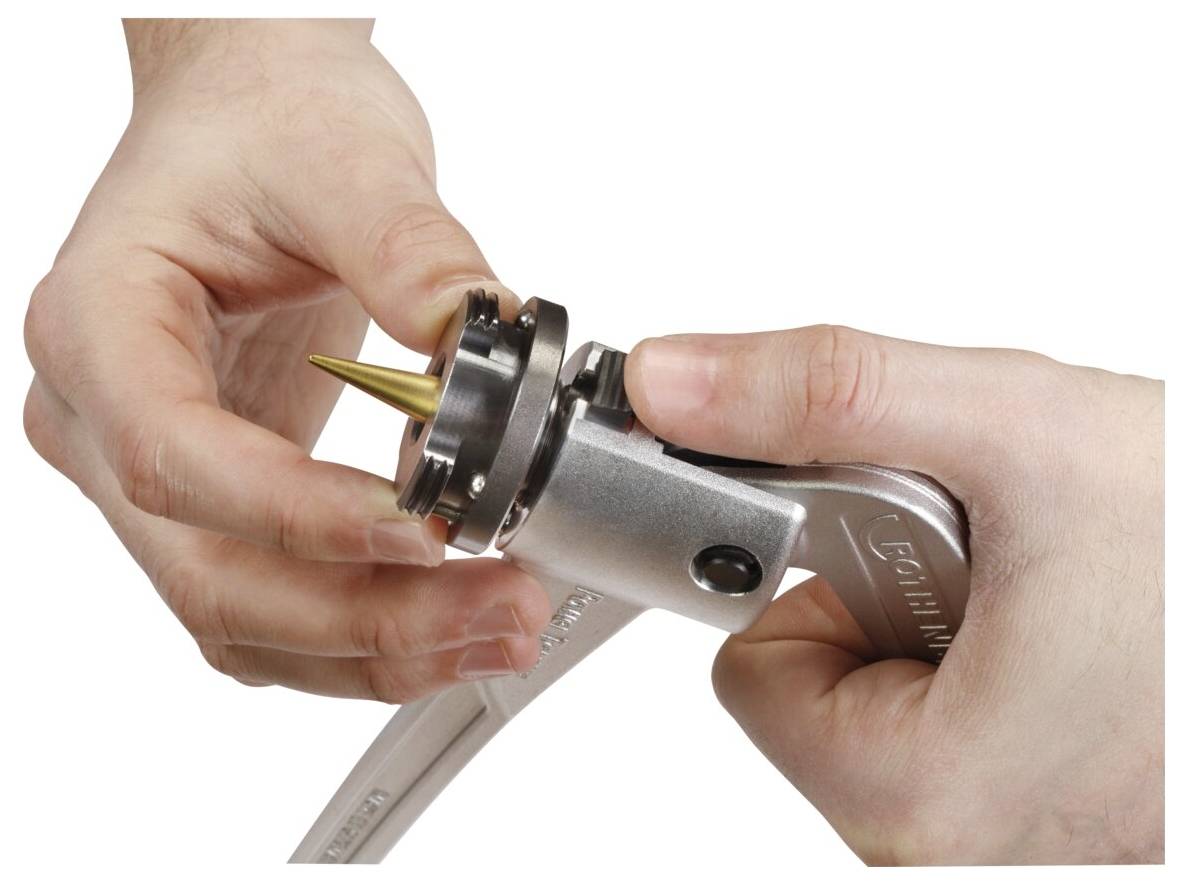 'Person holding a metal tool with a sharp, gold-colored tip, adjusting or assembling it using both hands.'