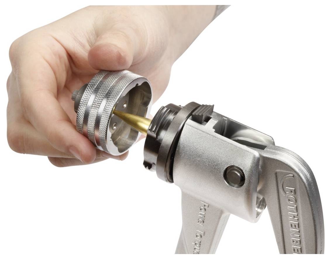 A hand gripping a metal tool with a shell holder in place, preparing it for reloading or adjusting. The setting suggests technical work.