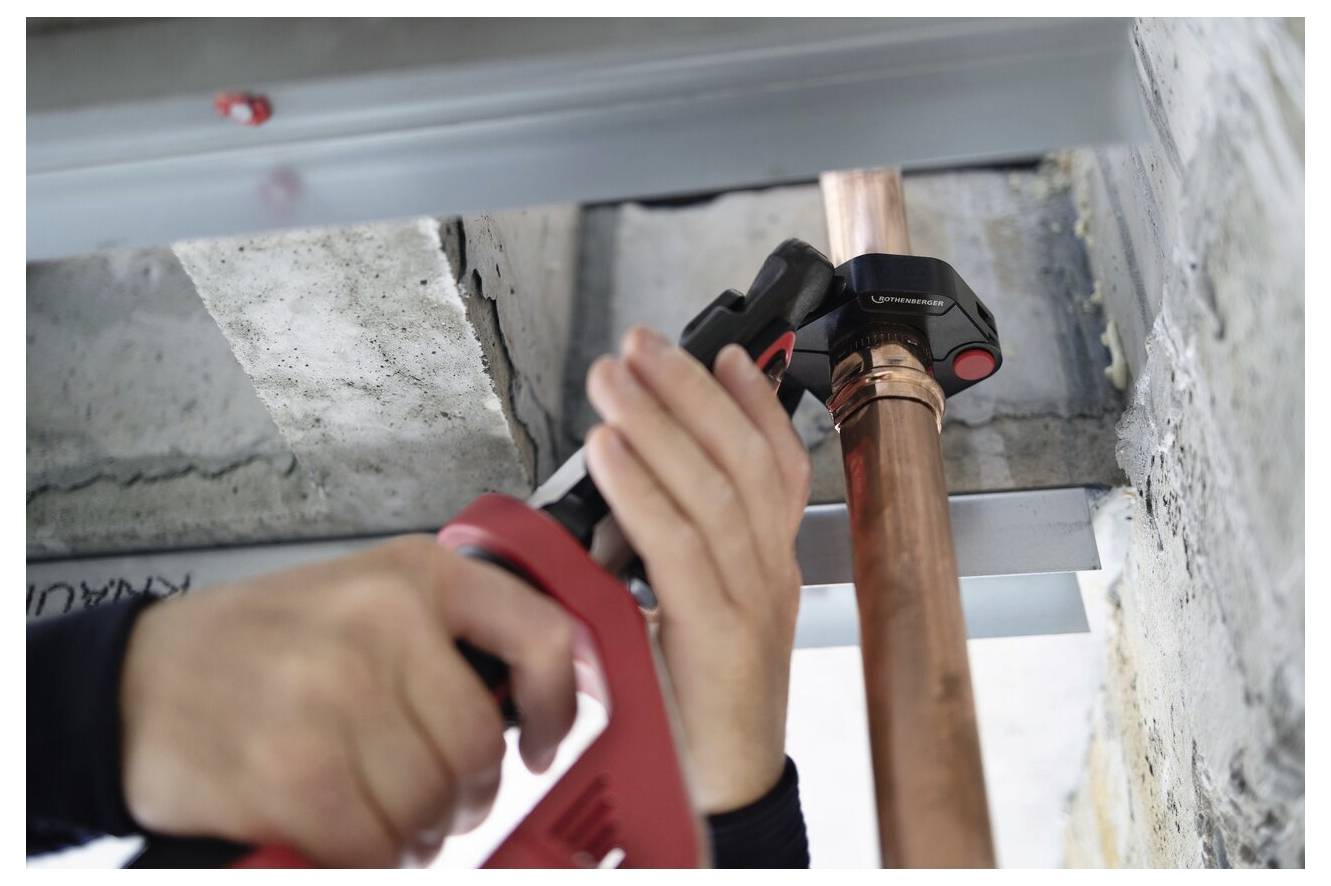 'Person using a tool to secure a copper pipe against a concrete ceiling.'
