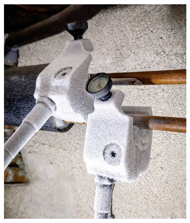 Frozen pipes covered in ice, with a pressure gauge attached to a plumbing valve outdoors.